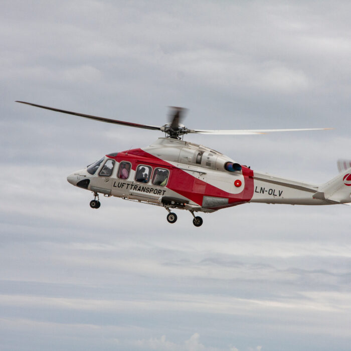 A red and white helicopter with "LUFTTRANSPORT" written on the side is flying in a cloudy sky.