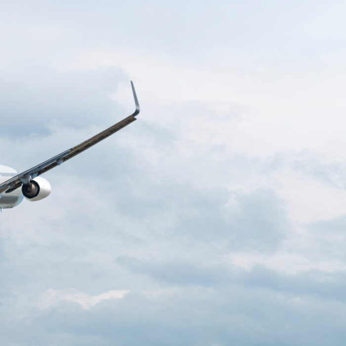 A commercial airplane is flying upward into a cloudy sky, viewed from behind and slightly below.