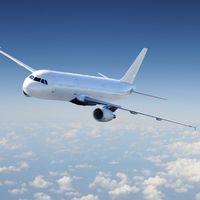 A commercial airplane flies above the clouds against a blue sky.