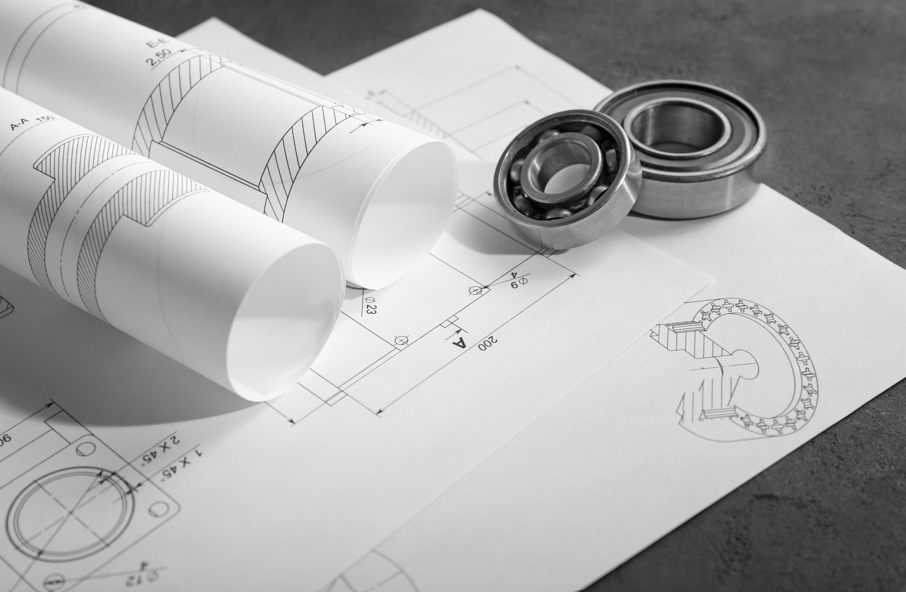 Rolled mechanical blueprints and ball bearings placed on technical drawings, illustrating engineering and manufacturing concepts.