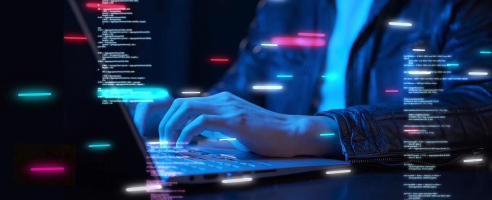 A person in a dark jacket types on a laptop with floating digital code and neon light effects overlaid on the image.