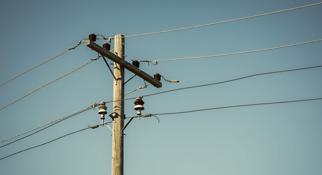 Wooden utility pole with ceramic insulators supporting power lines against a clear blue sky.