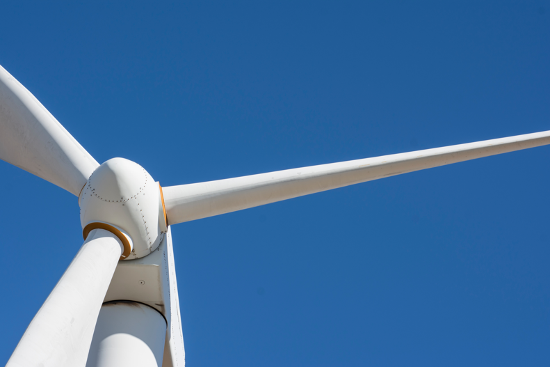 Close-up view of a white wind turbine with three blades set against a clear blue sky.